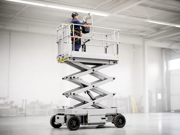Elektrische Scherenarbeitsbühne in einer Werkshalle, auf der ein Handwerker eine Deckenleuchte montiert